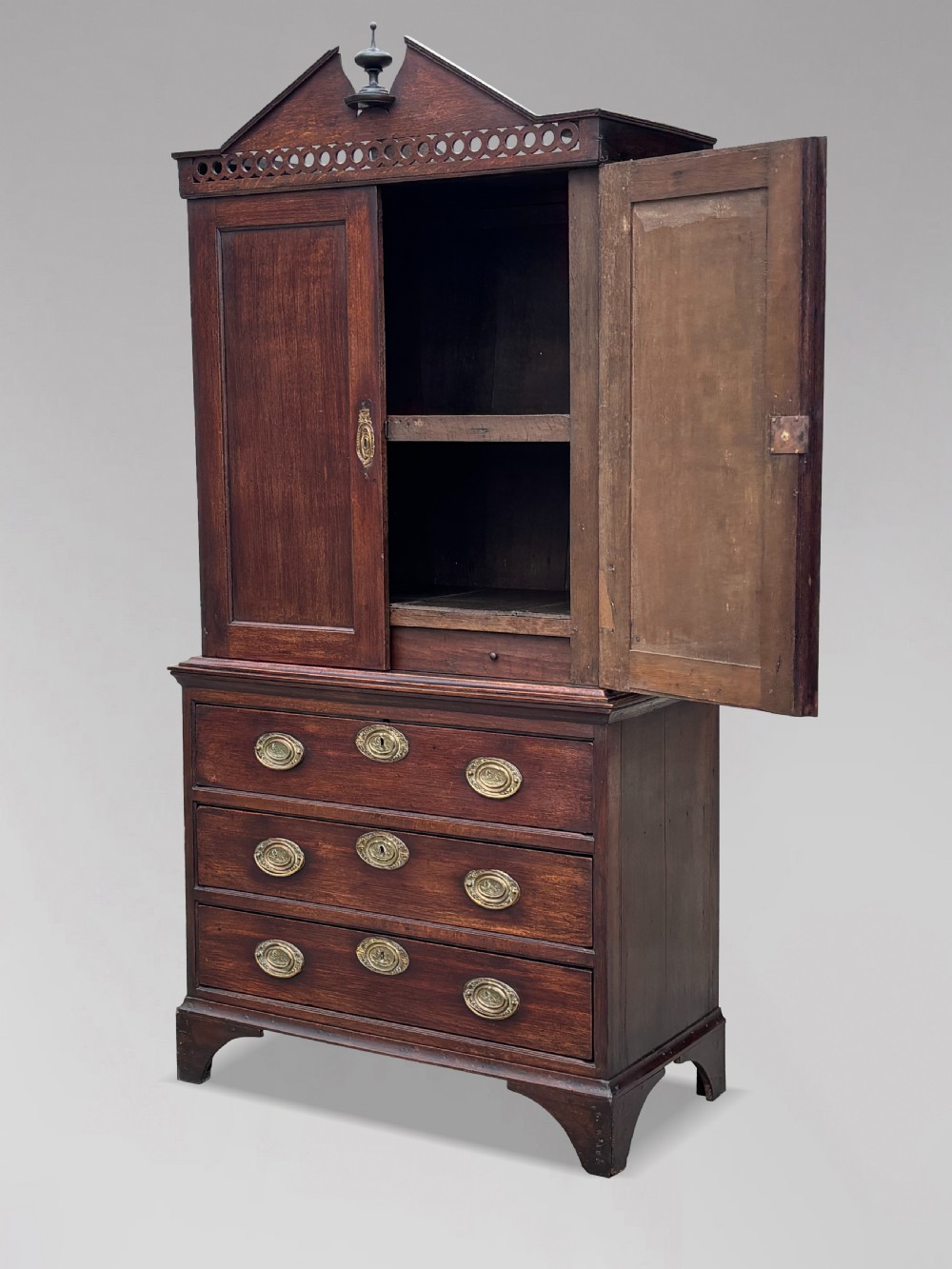 An 18th-century George III dark oak housekeepers cupboard featuring a fretwork gallery with a central turned finial, two upper panel doors, and three lower drawers with brass oval handles. View V