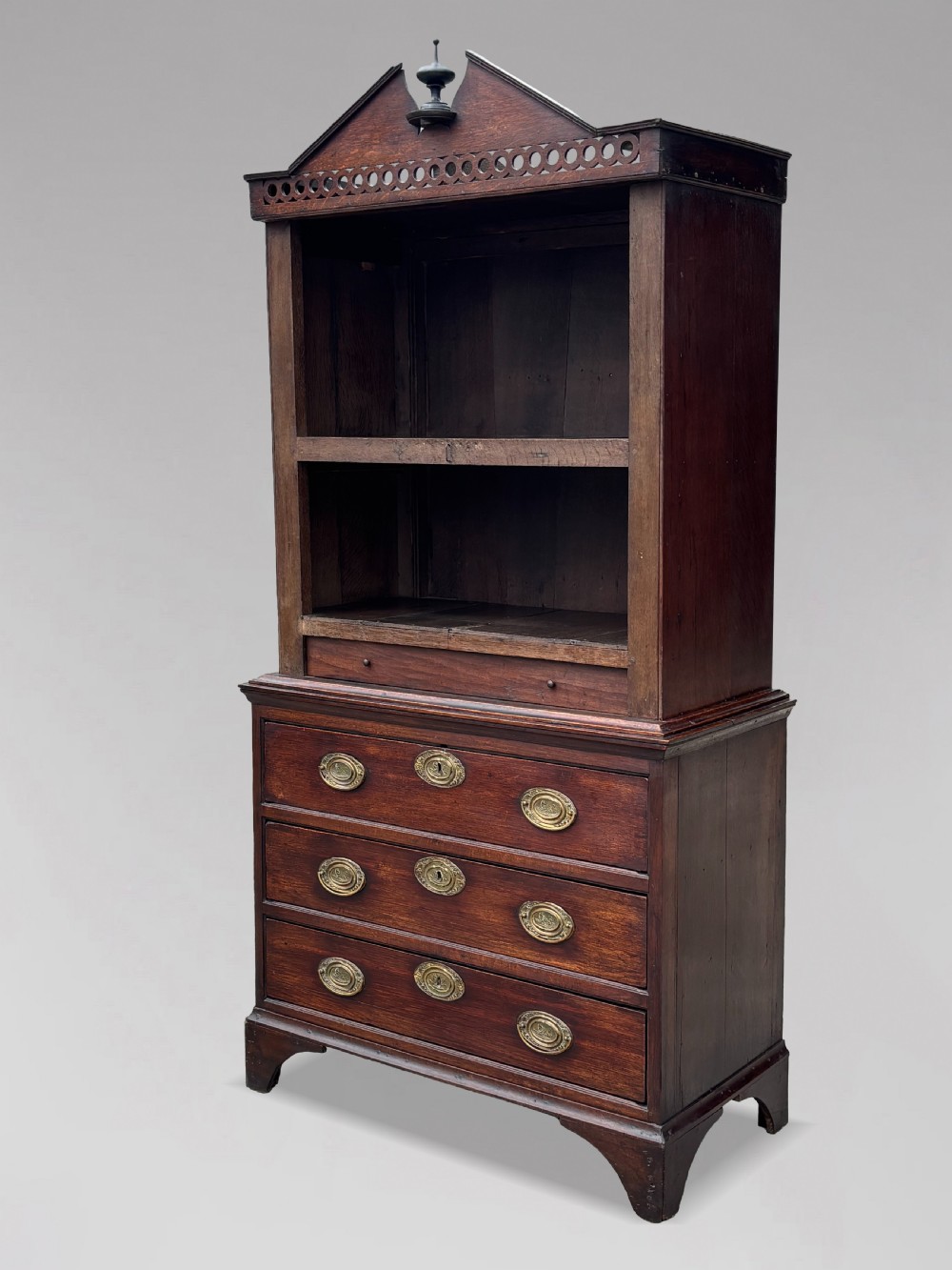 An 18th-century George III dark oak housekeepers cupboard featuring a fretwork gallery with a central turned finial, two upper panel doors, and three lower drawers with brass oval handles. View VI