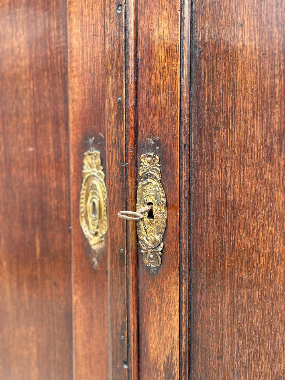 An 18th-century George III dark oak housekeepers cupboard featuring a fretwork gallery with a central turned finial, two upper panel doors, and three lower drawers with brass oval handles. View IX