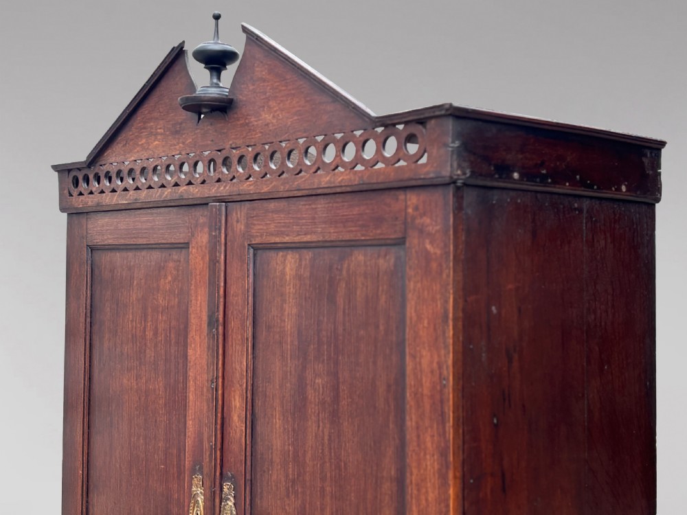 An 18th-century George III dark oak housekeepers cupboard featuring a fretwork gallery with a central turned finial, two upper panel doors, and three lower drawers with brass oval handles. View XII