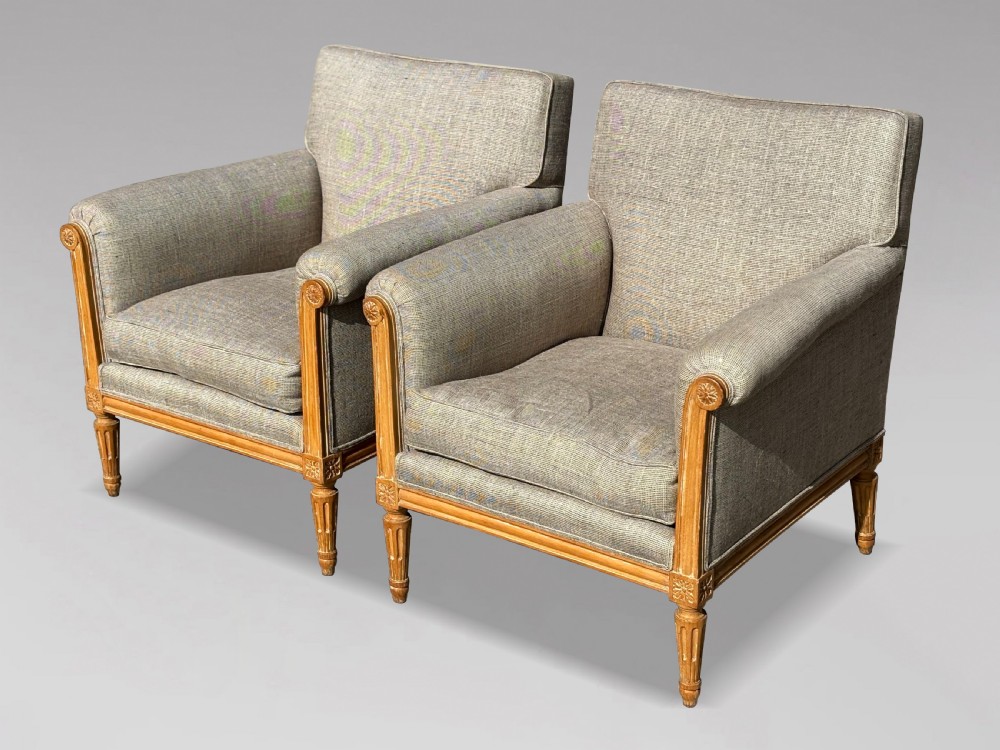 A pair of 19th-century French Louis XVI style armchairs featuring carved wooden frames, fluted legs, and neutral grey woven upholstery.