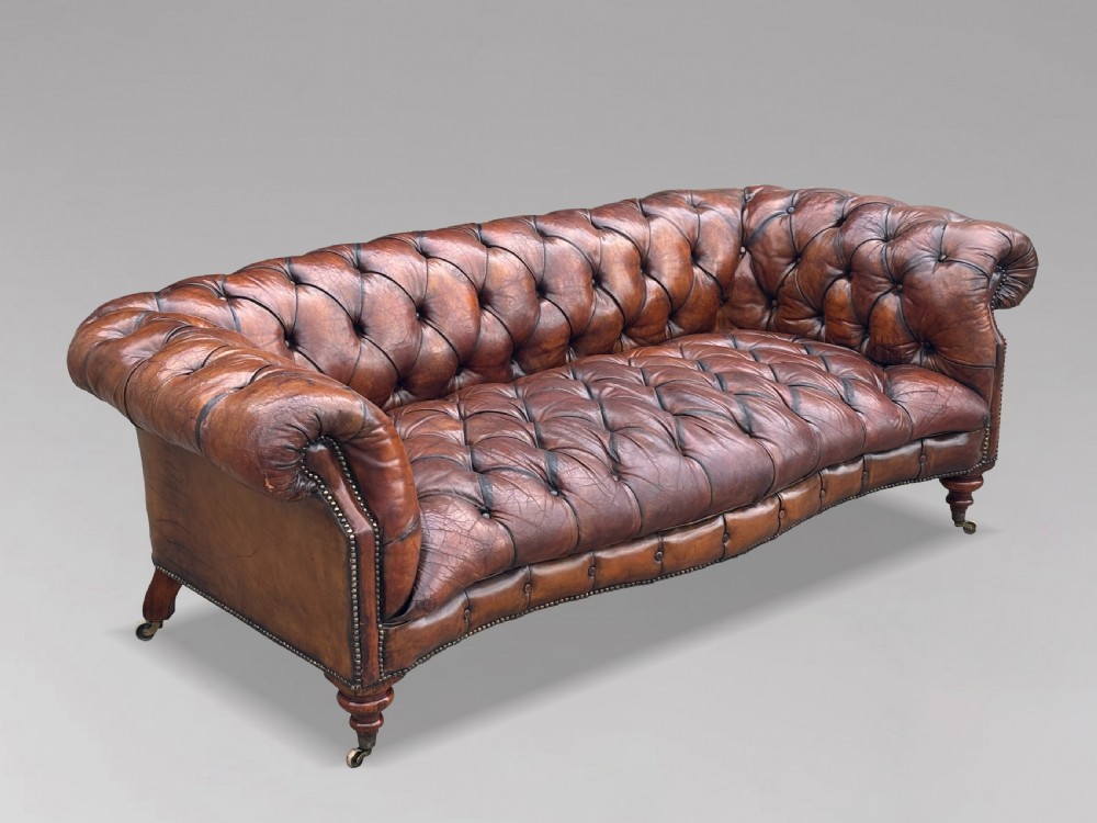 A late 19th-century Victorian brown leather Chesterfield sofa featuring deep buttoned upholstery, rolled arms, close studding, and turned legs with brass castors.