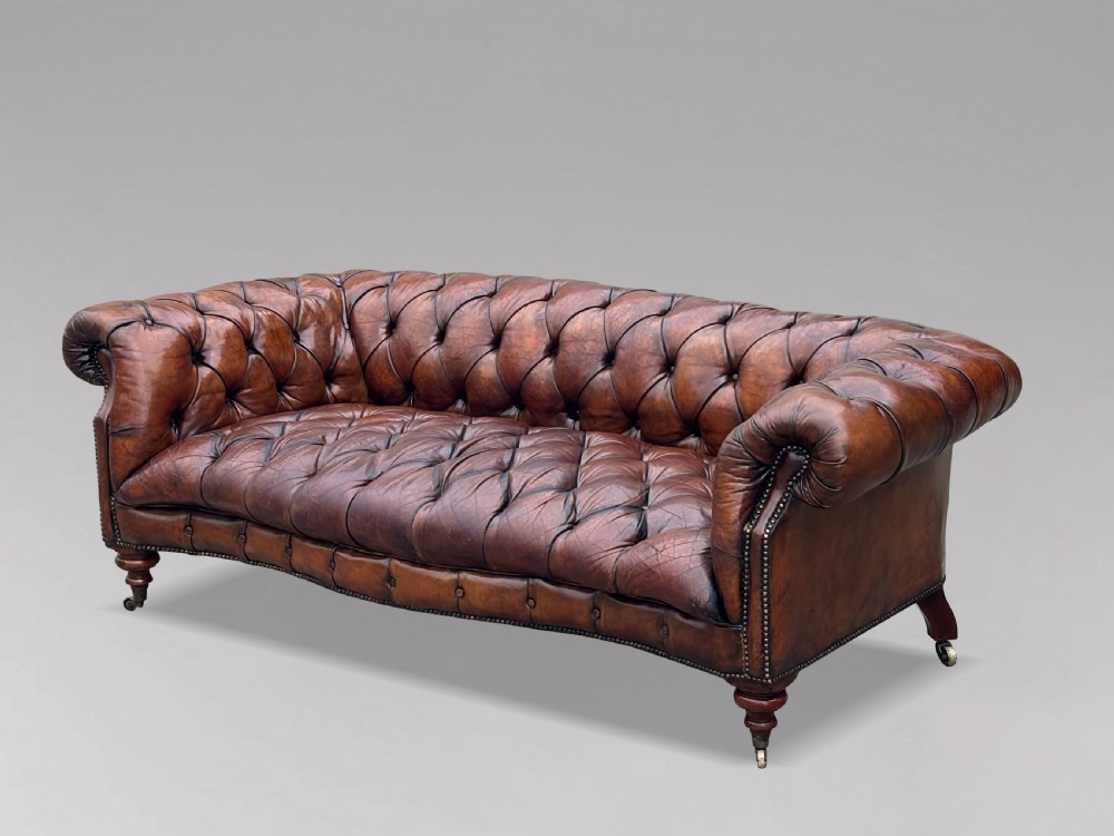 A late 19th-century Victorian brown leather Chesterfield sofa featuring deep buttoned upholstery, rolled arms, close studding, and turned legs with brass castors. View II
