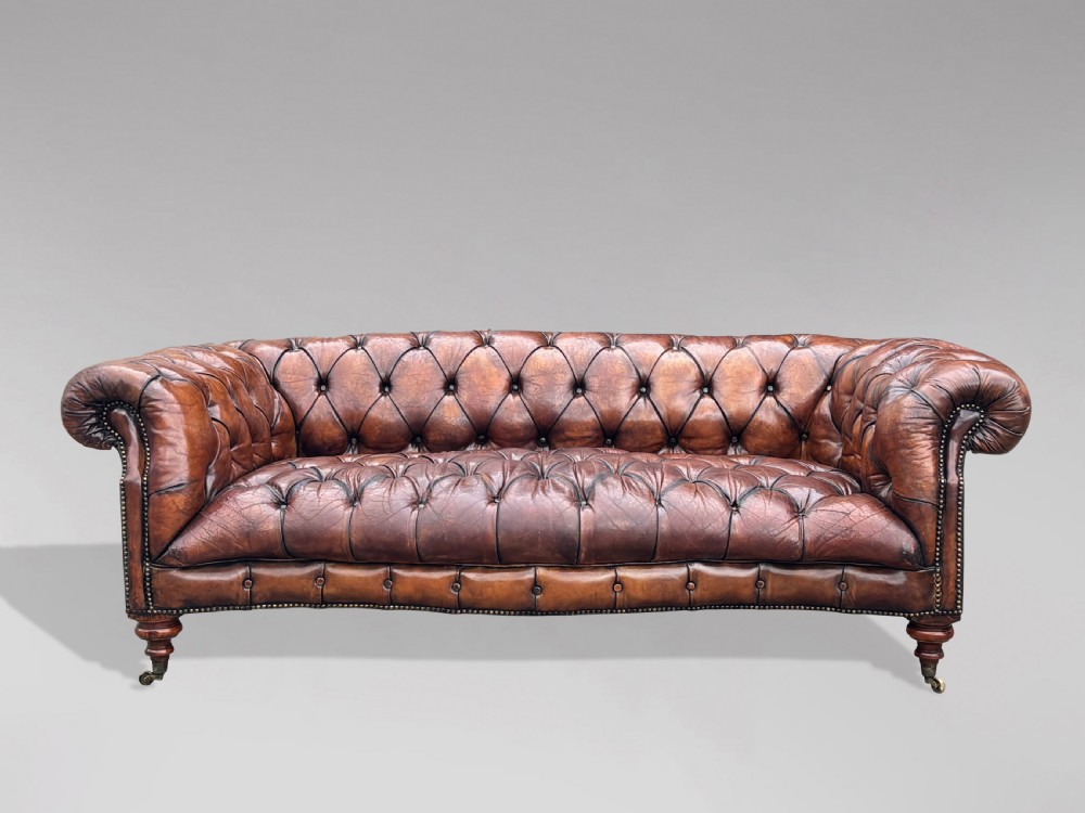 A late 19th-century Victorian brown leather Chesterfield sofa featuring deep buttoned upholstery, rolled arms, close studding, and turned legs with brass castors. View III