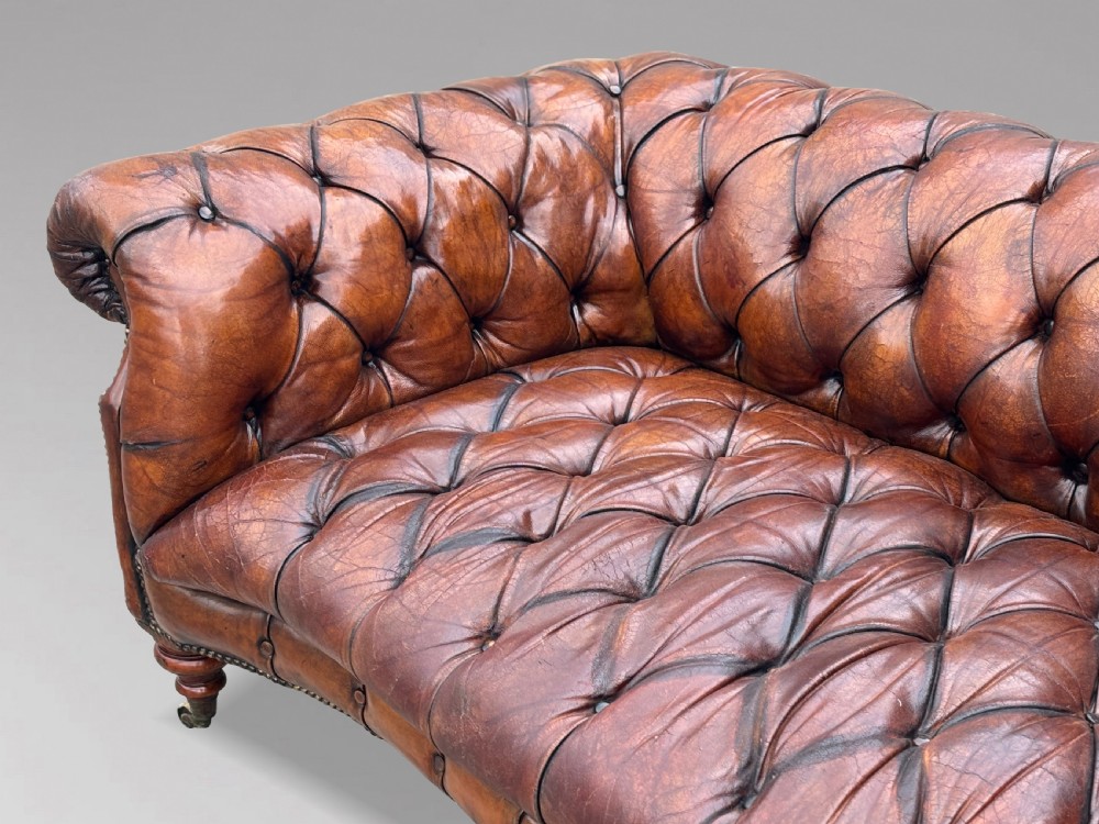 A late 19th-century Victorian brown leather Chesterfield sofa featuring deep buttoned upholstery, rolled arms, close studding, and turned legs with brass castors. View V