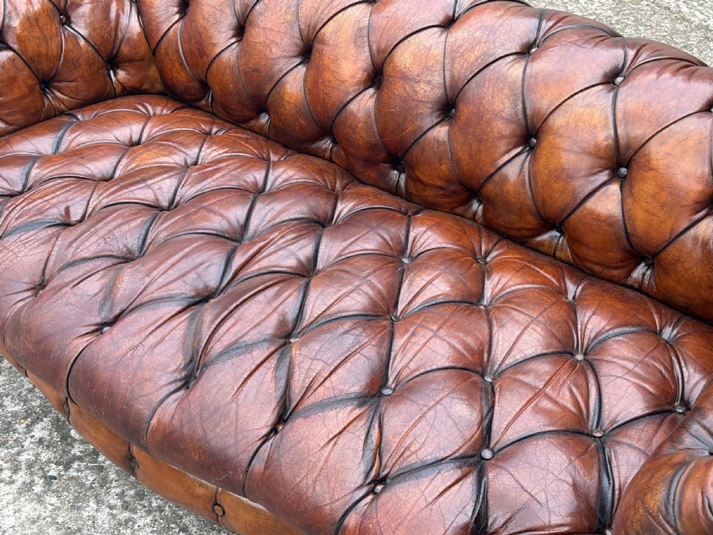 A late 19th-century Victorian brown leather Chesterfield sofa featuring deep buttoned upholstery, rolled arms, close studding, and turned legs with brass castors. View VII