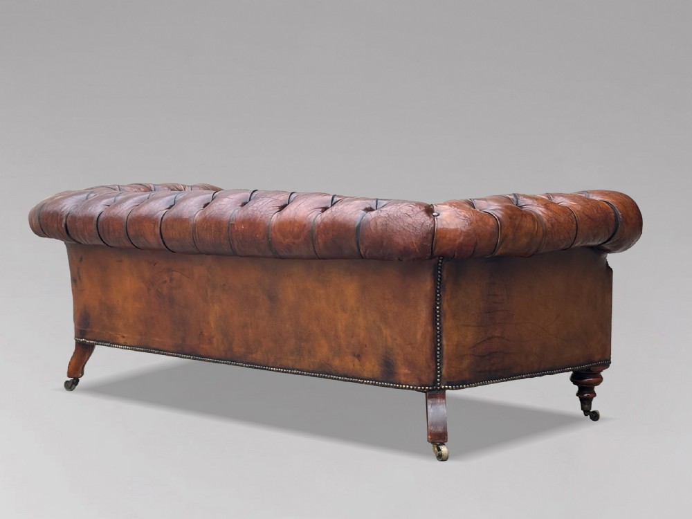 A late 19th-century Victorian brown leather Chesterfield sofa featuring deep buttoned upholstery, rolled arms, close studding, and turned legs with brass castors. View VIII
