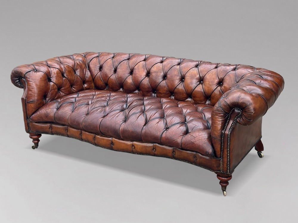 A late 19th-century Victorian brown leather Chesterfield sofa featuring deep buttoned upholstery, rolled arms, close studding, and turned legs with brass castors. View IX