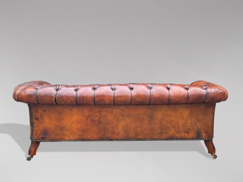 A late 19th-century Victorian brown leather Chesterfield sofa featuring deep buttoned upholstery, rolled arms, close studding, and turned legs with brass castors. View XI