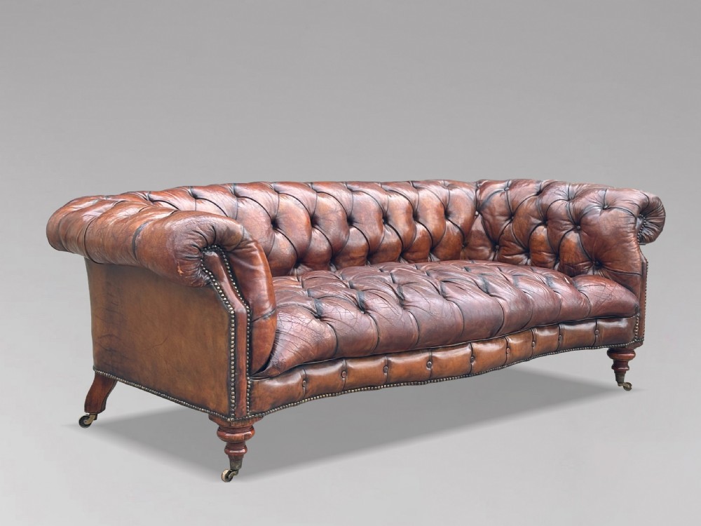 A late 19th-century Victorian brown leather Chesterfield sofa featuring deep buttoned upholstery, rolled arms, close studding, and turned legs with brass castors. View XII
