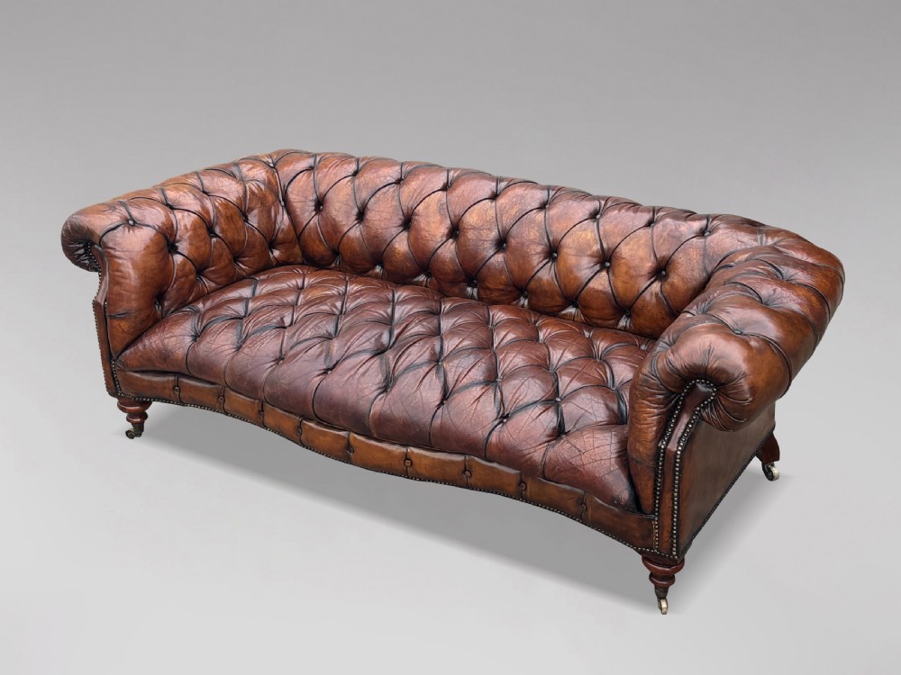A late 19th-century Victorian brown leather Chesterfield sofa featuring deep buttoned upholstery, rolled arms, close studding, and turned legs with brass castors. View XIII