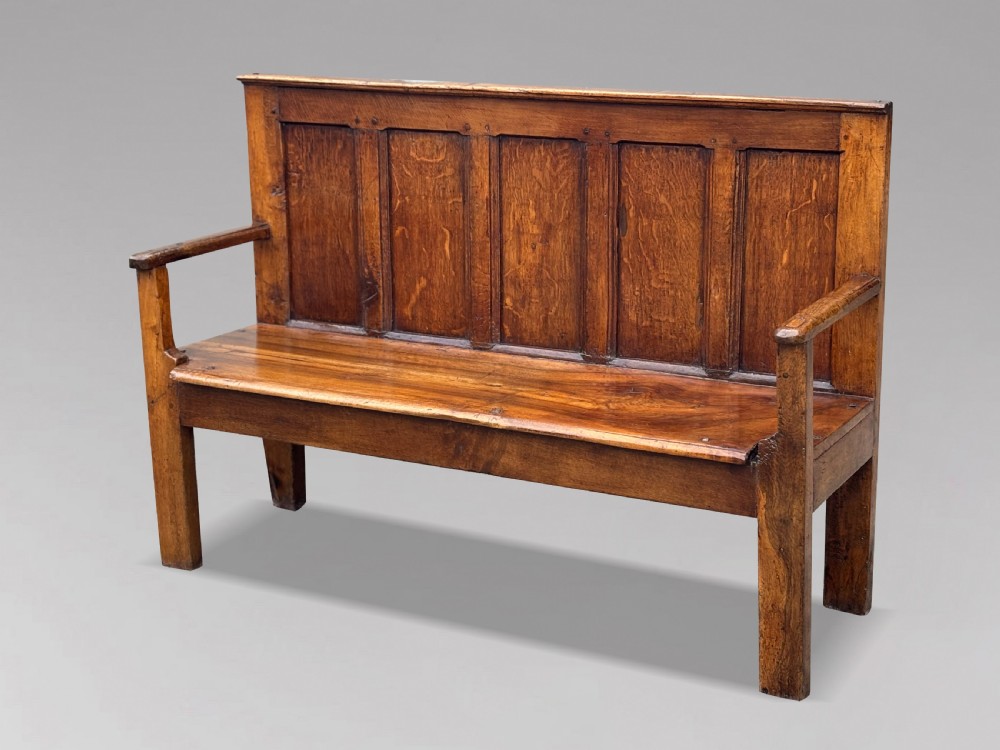An 18th-century Georgian high-back settle crafted from oak and elm featuring a panelled back and wooden armrests.