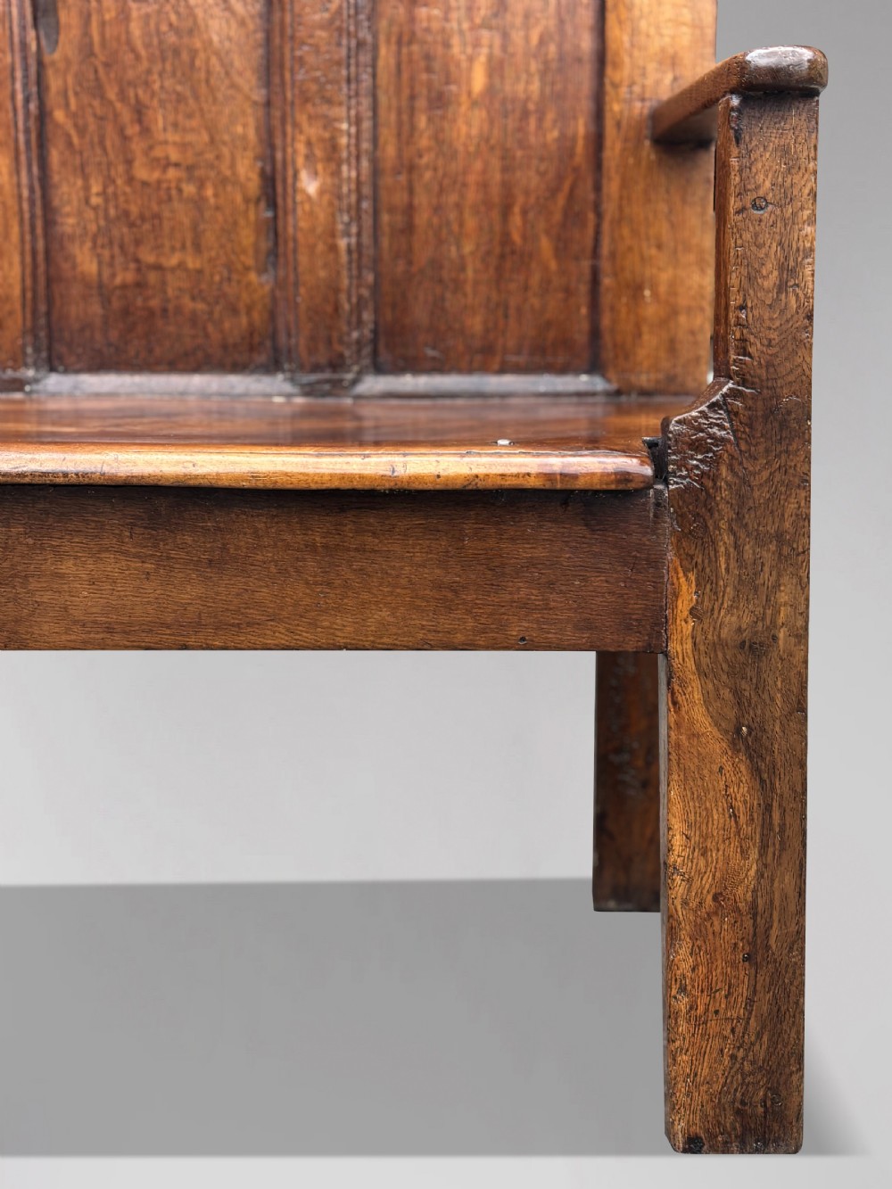An 18th-century Georgian high-back settle crafted from oak and elm featuring a panelled back and wooden armrests. View V