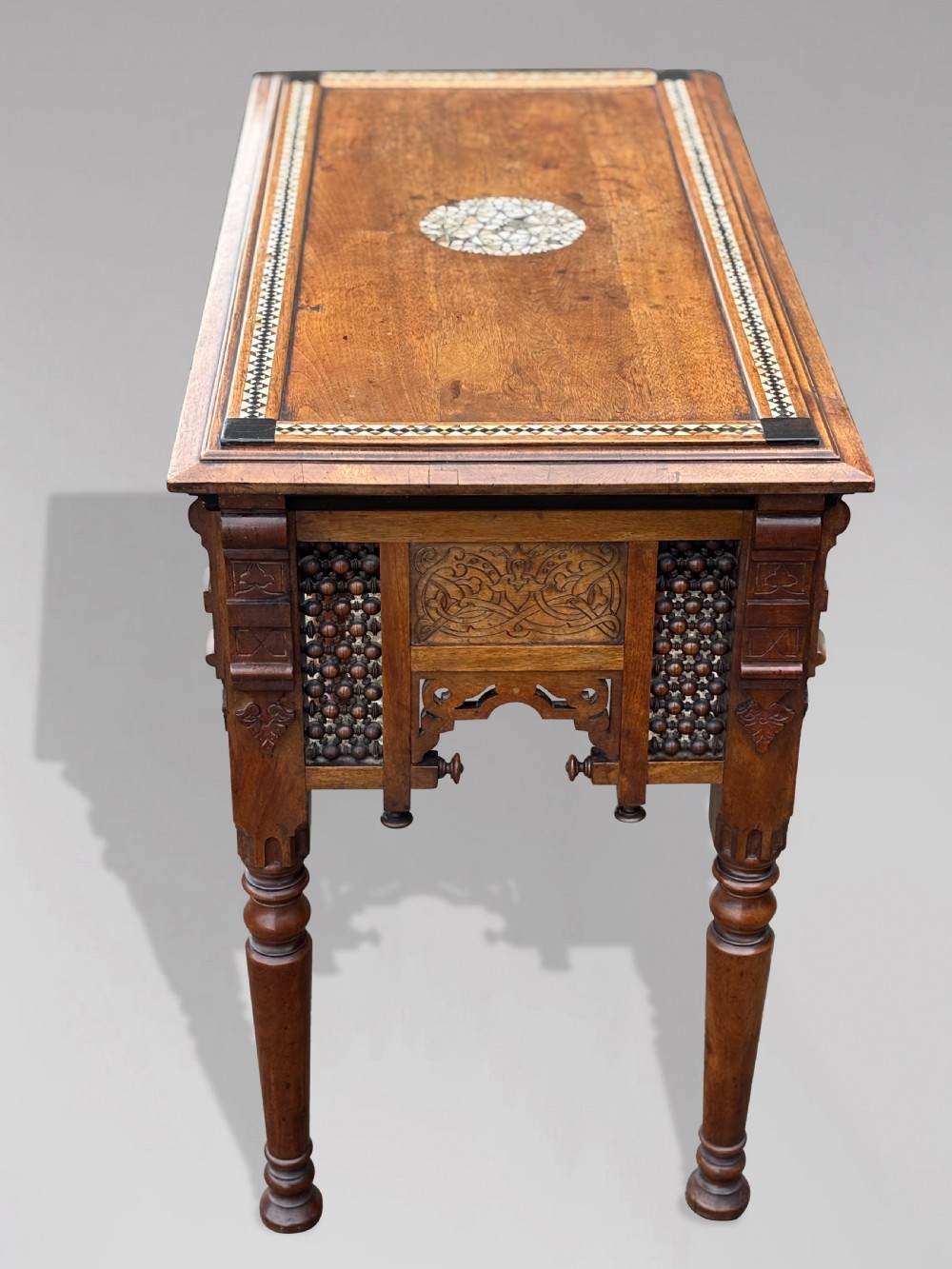 A late 19th-century Aesthetic Movement side table featuring carved wood, a central mother-of-pearl inlay medallion, turned spindle side panels, and turned legs. View X