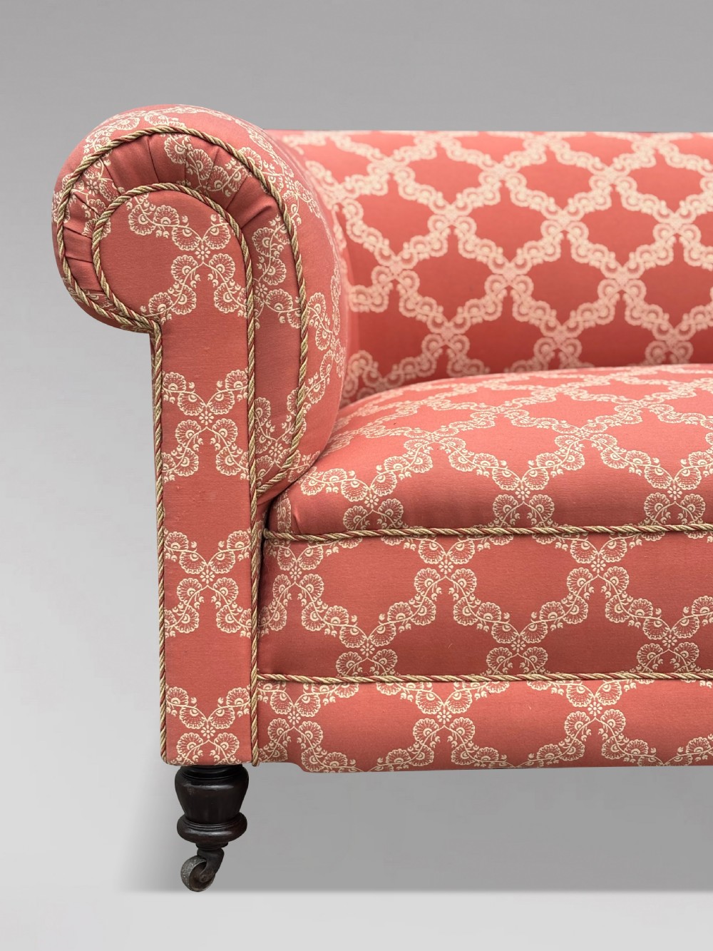 A 19th-century Victorian upholstered sofa featuring terracotta and cream patterned fabric, rolled arms, and dark turned wooden legs on brass castors. View IV
