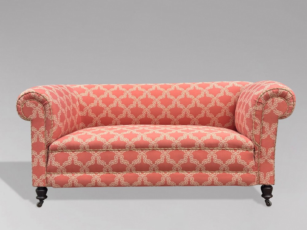 A 19th-century Victorian upholstered sofa featuring terracotta and cream patterned fabric, rolled arms, and dark turned wooden legs on brass castors. View V