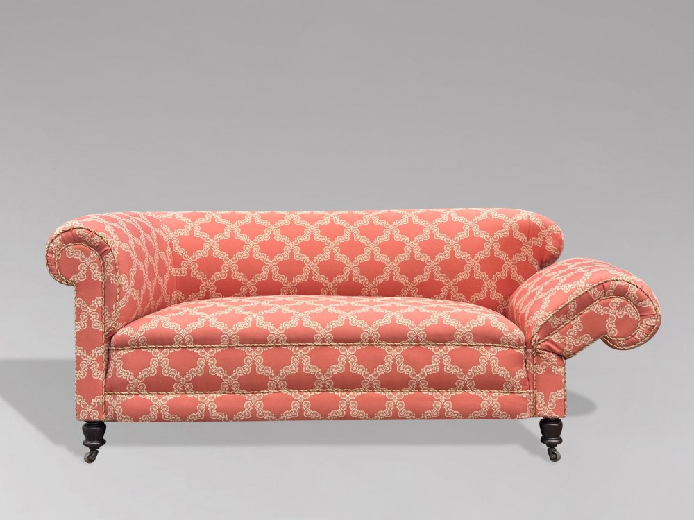 A 19th-century Victorian upholstered sofa featuring terracotta and cream patterned fabric, rolled arms, and dark turned wooden legs on brass castors. View VI