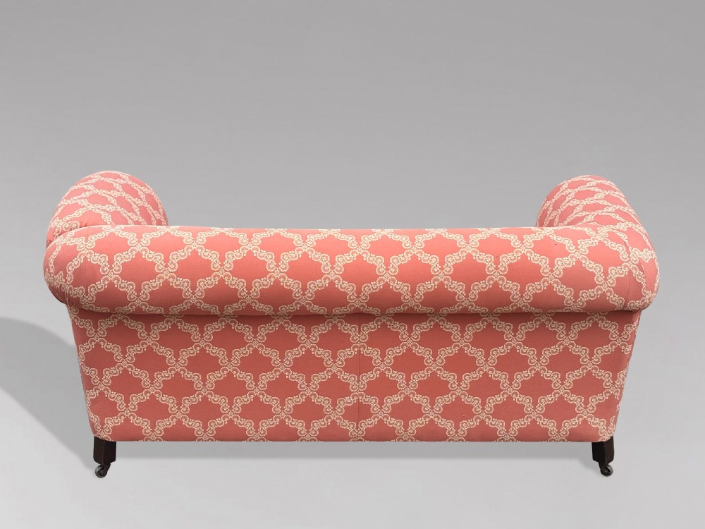 A 19th-century Victorian upholstered sofa featuring terracotta and cream patterned fabric, rolled arms, and dark turned wooden legs on brass castors. View VII
