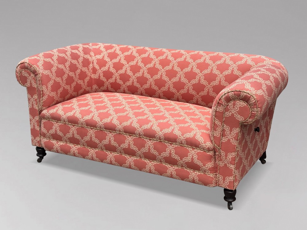 A 19th-century Victorian upholstered sofa featuring terracotta and cream patterned fabric, rolled arms, and dark turned wooden legs on brass castors. View X