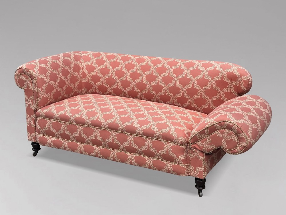A 19th-century Victorian upholstered sofa featuring terracotta and cream patterned fabric, rolled arms, and dark turned wooden legs on brass castors.