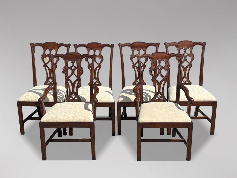 A set of six Edwardian mahogany dining chairs featuring pierced carved back splats, serpentine top rails, cream upholstered seats, and straight square legs with H-stretchers.