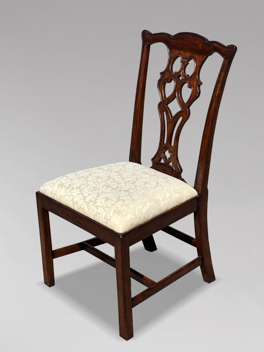 A set of six Edwardian mahogany dining chairs featuring pierced carved back splats, serpentine top rails, cream upholstered seats, and straight square legs with H-stretchers. View IV