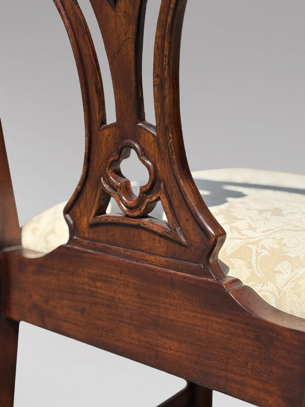 A set of six Edwardian mahogany dining chairs featuring pierced carved back splats, serpentine top rails, cream upholstered seats, and straight square legs with H-stretchers. View VII
