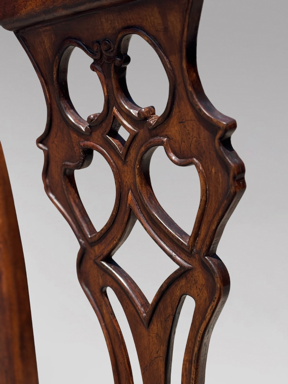 A set of six Edwardian mahogany dining chairs featuring pierced carved back splats, serpentine top rails, cream upholstered seats, and straight square legs with H-stretchers. View VIII