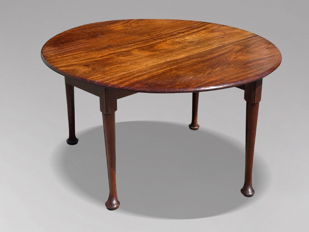 An 18th-century George II mahogany drop-leaf dining table with a round top and tapered legs ending in pad feet.