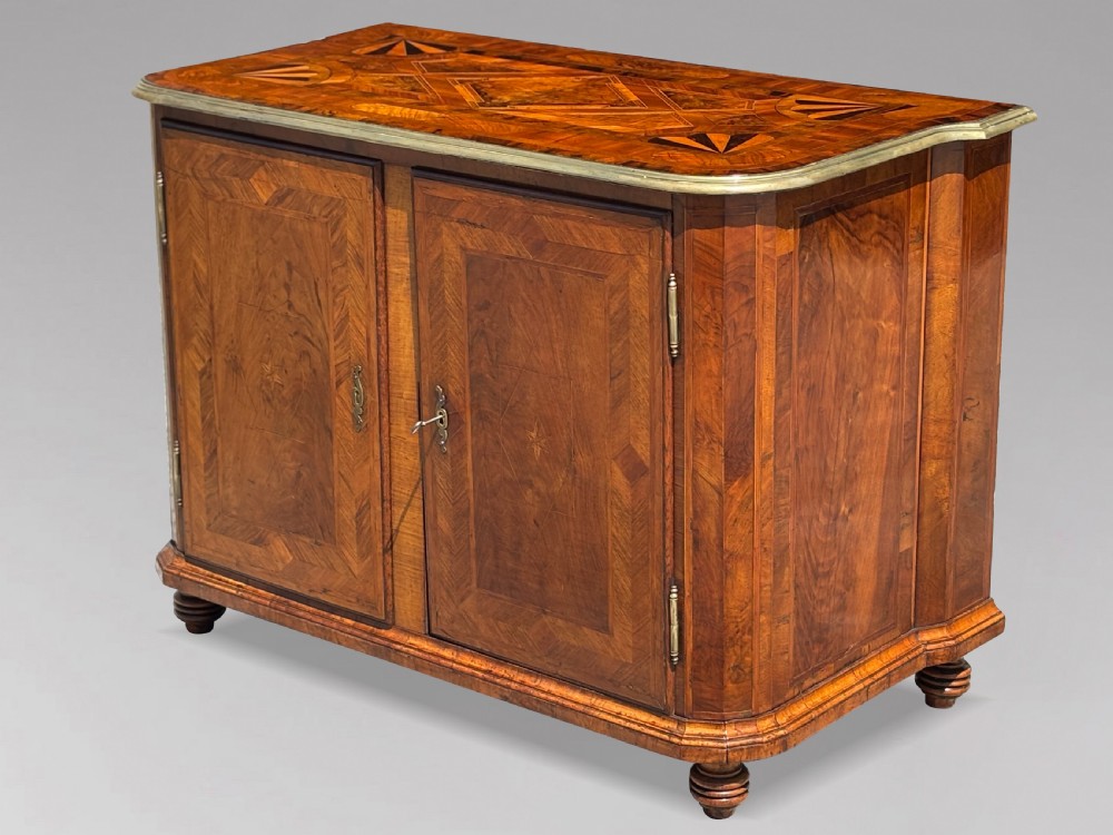 An 18th-century Maltese walnut cabinet with geometric parquetry inlays on the top and two panelled doors flanked by rounded corners on turned feet.