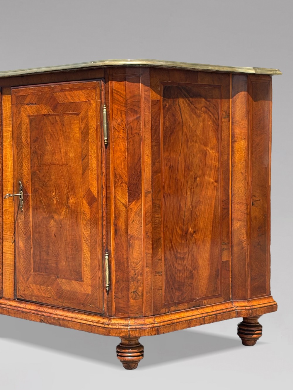 An 18th-century Maltese walnut cabinet with geometric parquetry inlays on the top and two panelled doors flanked by rounded corners on turned feet. View XII