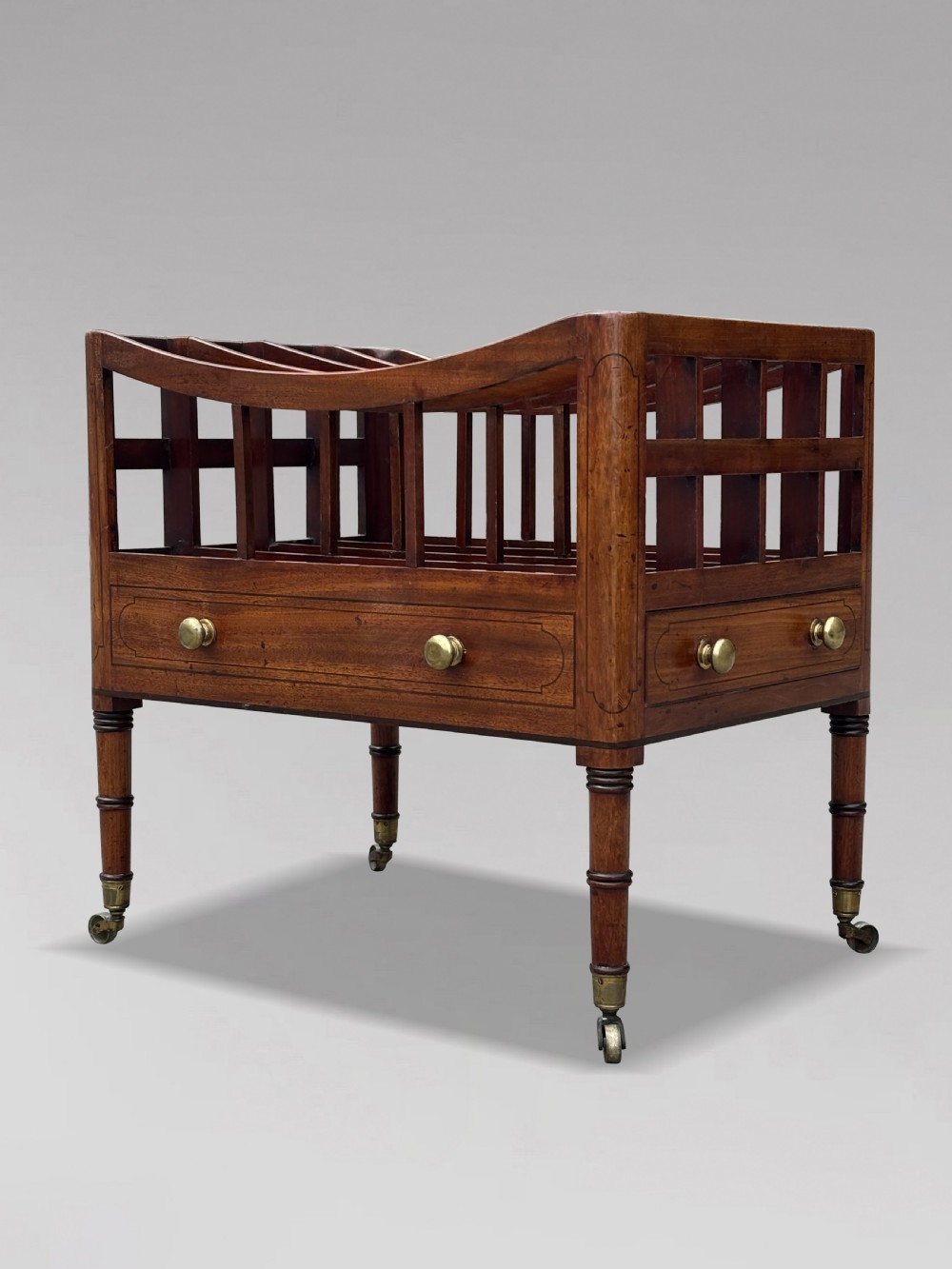 An 18th-century George III mahogany canterbury featuring slatted divisions, lower drawers with brass knobs, and turned legs on brass castors.