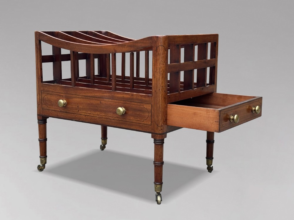An 18th-century George III mahogany canterbury featuring slatted divisions, lower drawers with brass knobs, and turned legs on brass castors. View IV