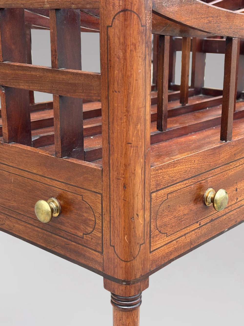 An 18th-century George III mahogany canterbury featuring slatted divisions, lower drawers with brass knobs, and turned legs on brass castors. View VI