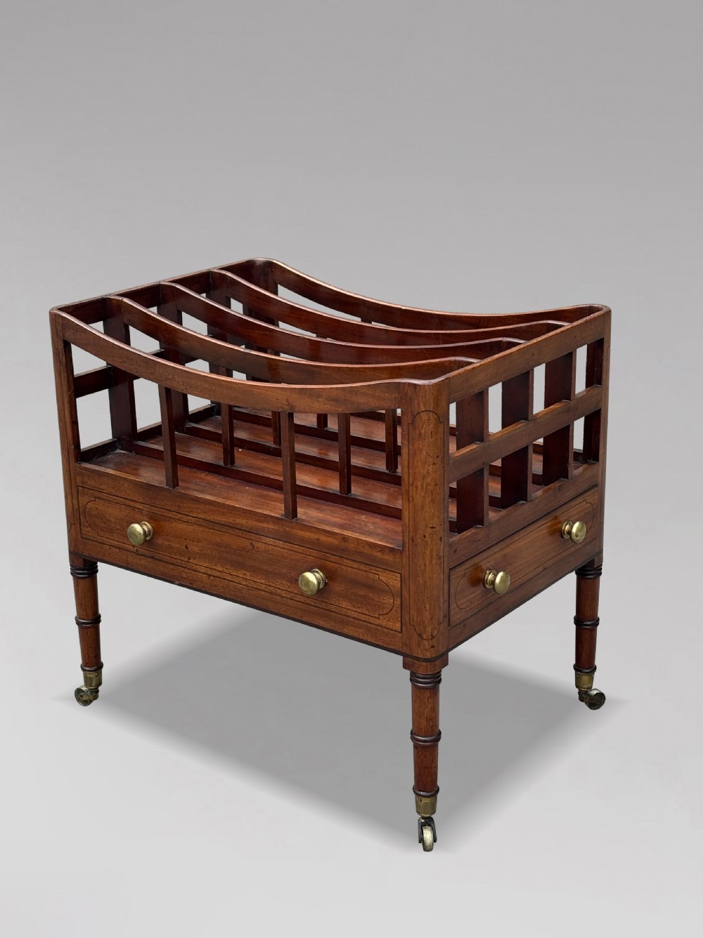 An 18th-century George III mahogany canterbury featuring slatted divisions, lower drawers with brass knobs, and turned legs on brass castors. View VIII