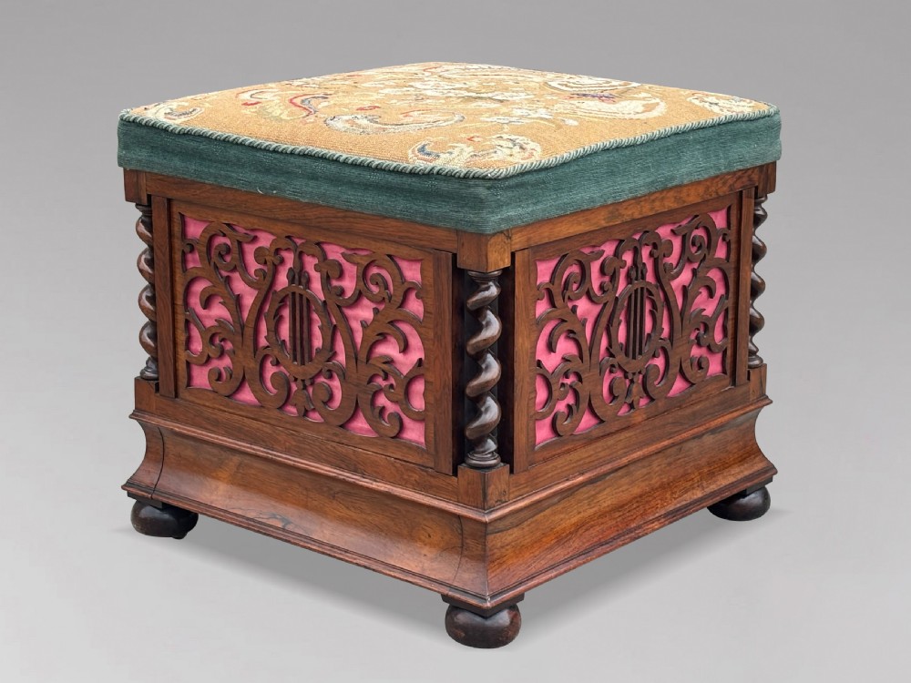 A Victorian rosewood piano stool featuring a square tapestry-upholstered top with green velvet edging, carved fretwork side panels, corner barley twist columns, and bun feet.