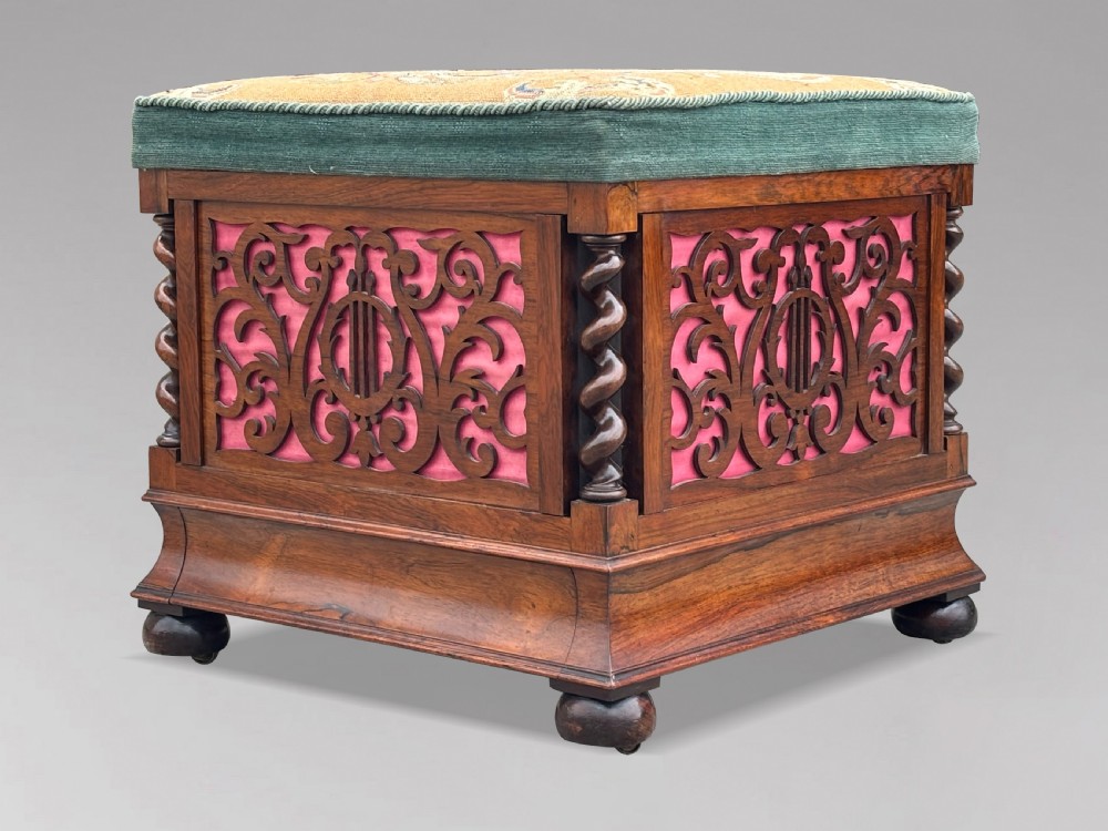 A Victorian rosewood piano stool featuring a square tapestry-upholstered top with green velvet edging, carved fretwork side panels, corner barley twist columns, and bun feet. View II