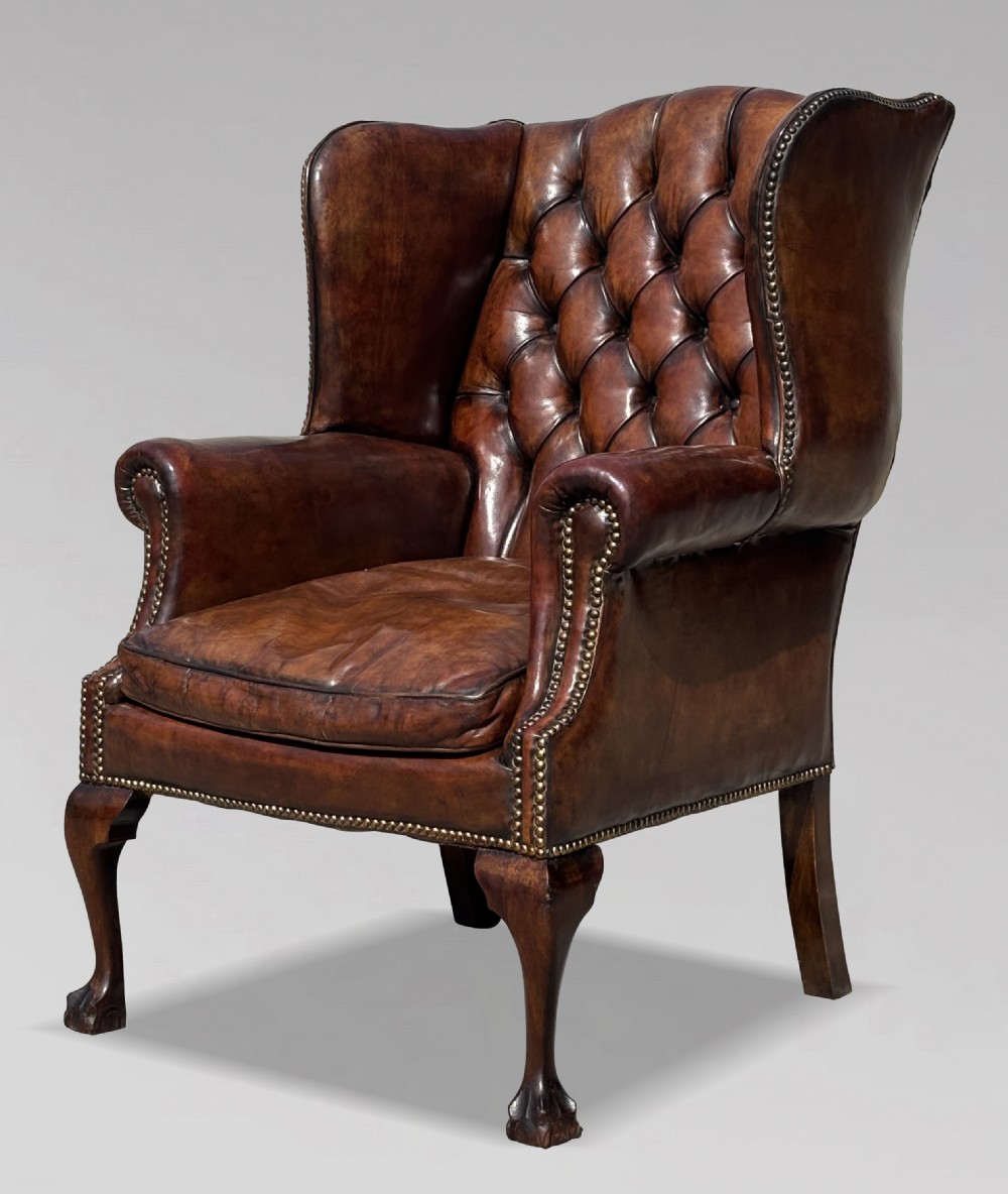 Late Victorian brown leather wingback armchair with deep buttoned tufting, brass studding detail, and carved mahogany cabriole legs.
