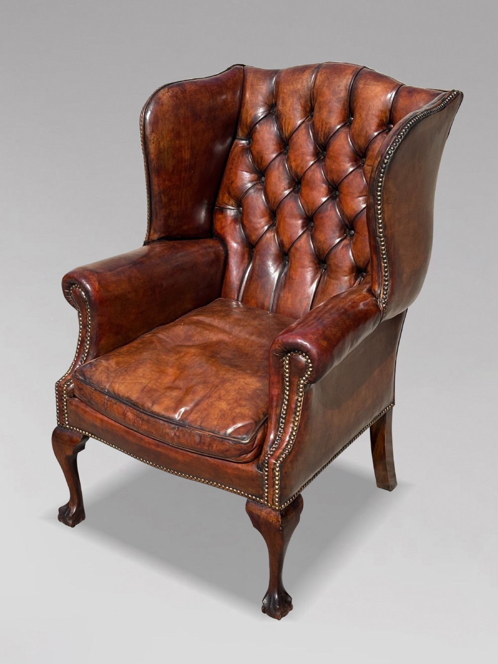 Late Victorian brown leather wingback armchair with deep buttoned tufting, brass studding detail, and carved mahogany cabriole legs. View II