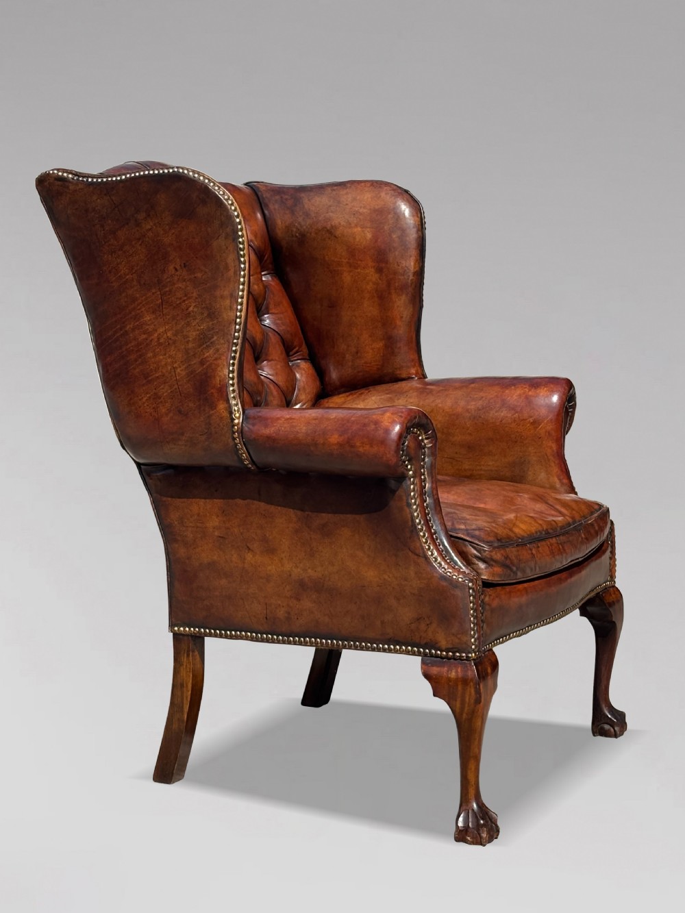Late Victorian brown leather wingback armchair with deep buttoned tufting, brass studding detail, and carved mahogany cabriole legs. View III