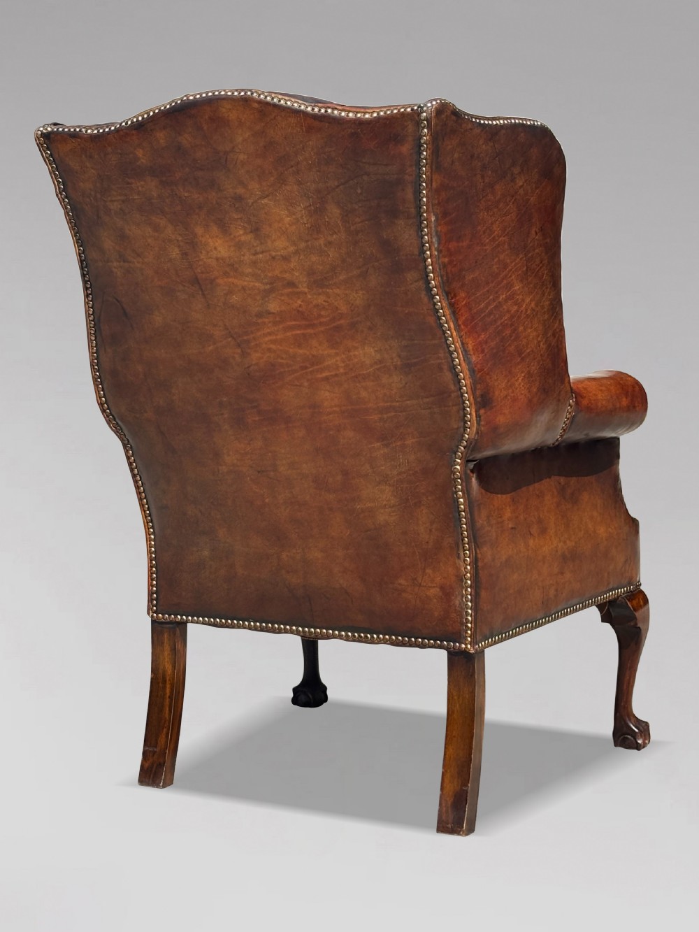 Late Victorian brown leather wingback armchair with deep buttoned tufting, brass studding detail, and carved mahogany cabriole legs. View IV