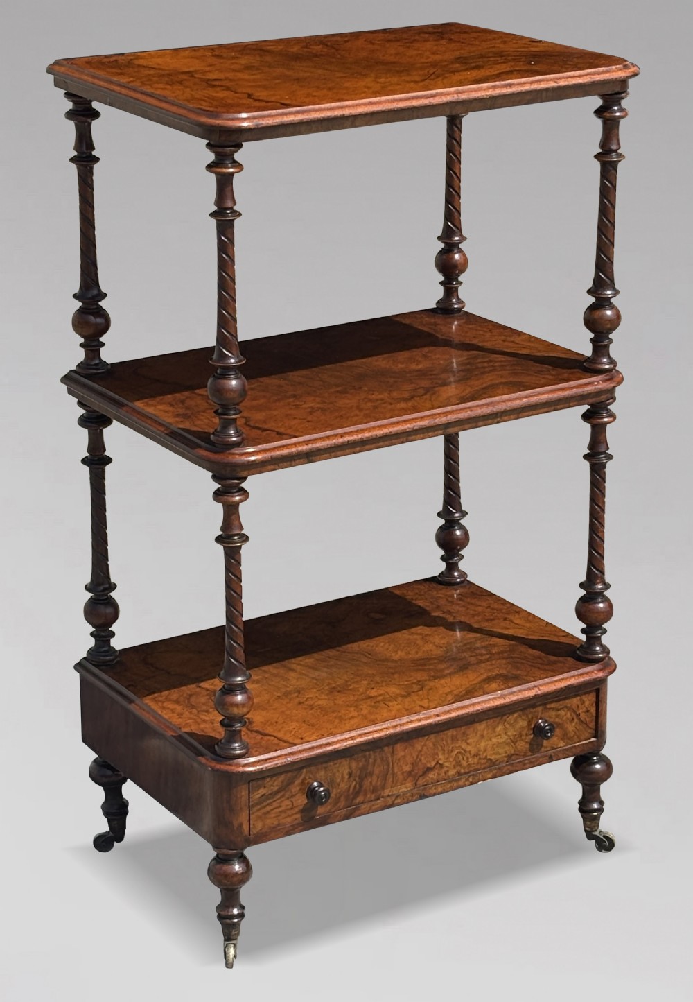 A Victorian walnut three-tier whatnot featuring barley twist supports, a single lower drawer, and brass castors.