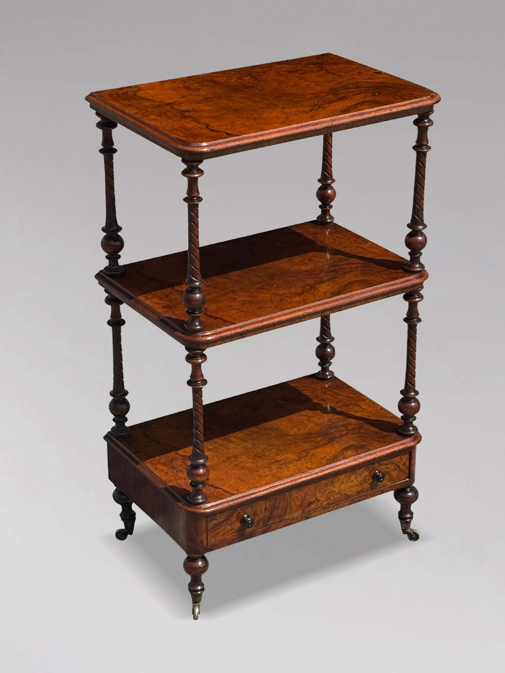 A Victorian walnut three-tier whatnot featuring barley twist supports, a single lower drawer, and brass castors. View II