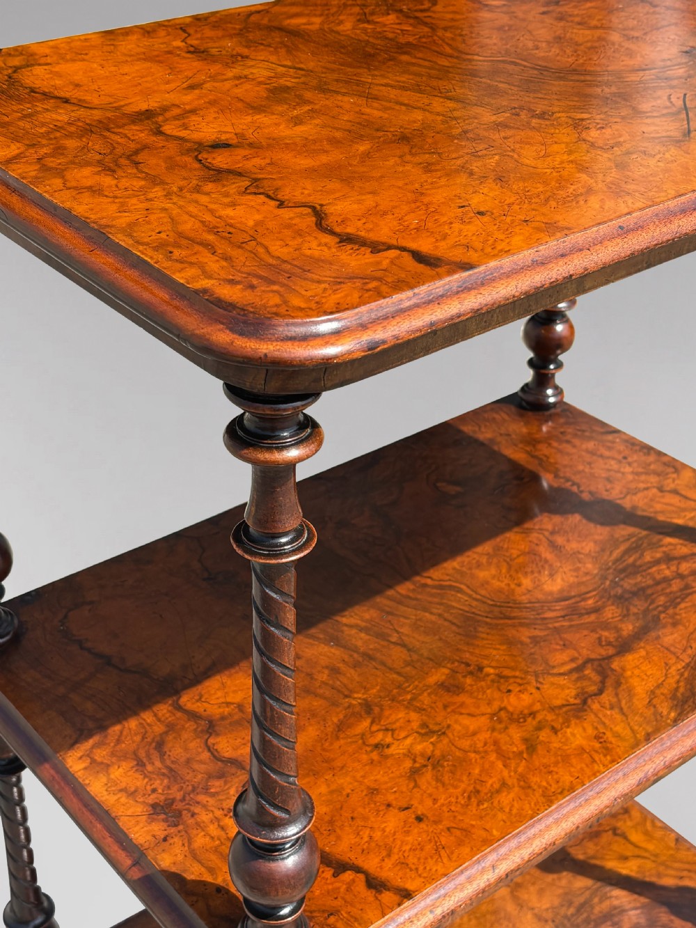 A Victorian walnut three-tier whatnot featuring barley twist supports, a single lower drawer, and brass castors. View V