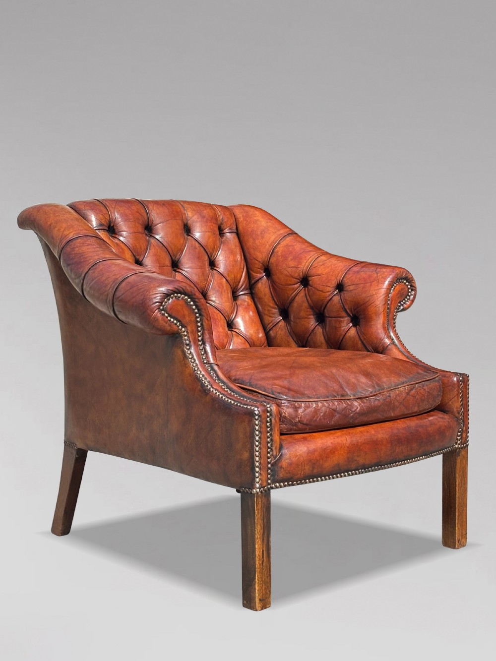 A nineteenth-century armchair upholstered in deep-buttoned brown leather with brass stud trimming along the arms and front rail, set on square wooden legs. View IV
