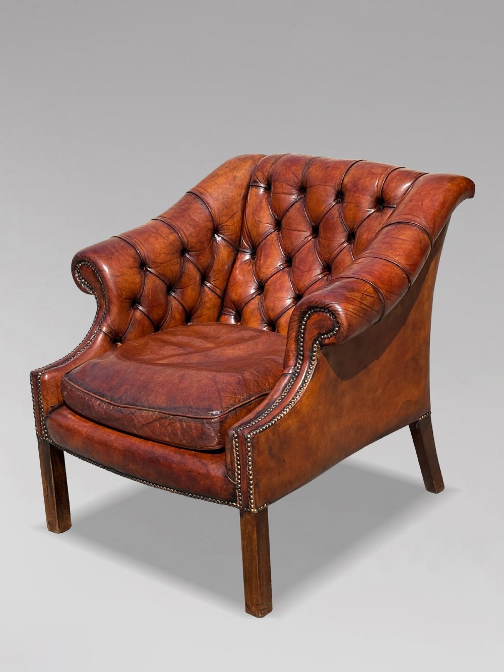 A nineteenth-century armchair upholstered in deep-buttoned brown leather with brass stud trimming along the arms and front rail, set on square wooden legs. View V
