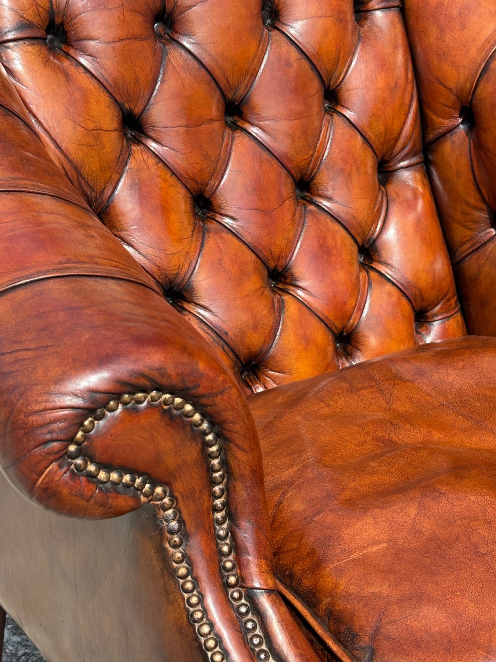 A nineteenth-century armchair upholstered in deep-buttoned brown leather with brass stud trimming along the arms and front rail, set on square wooden legs. View VI