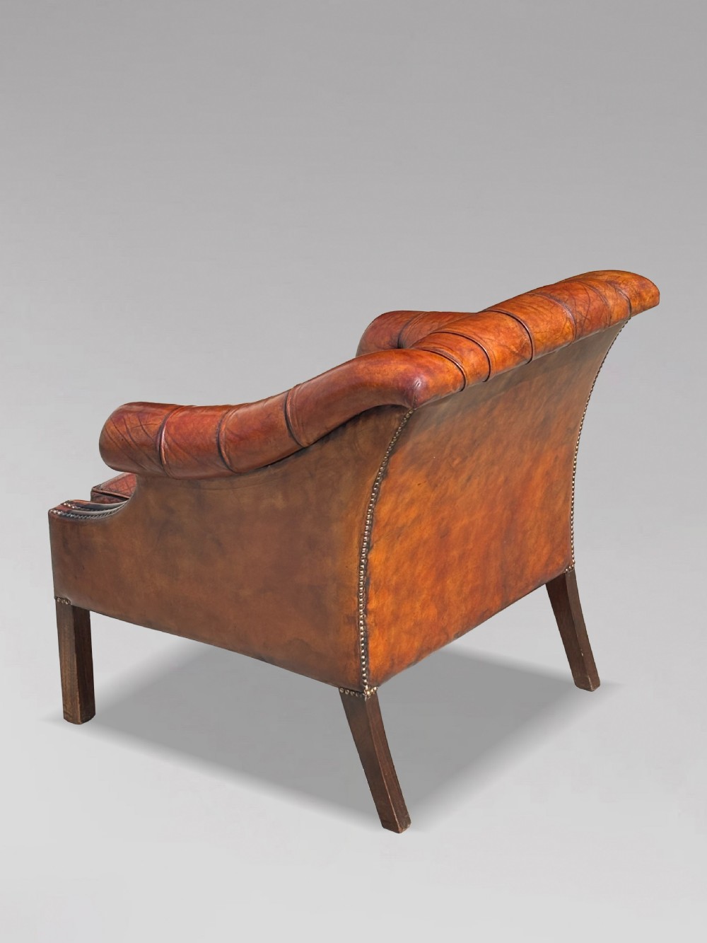 A nineteenth-century armchair upholstered in deep-buttoned brown leather with brass stud trimming along the arms and front rail, set on square wooden legs. View IX