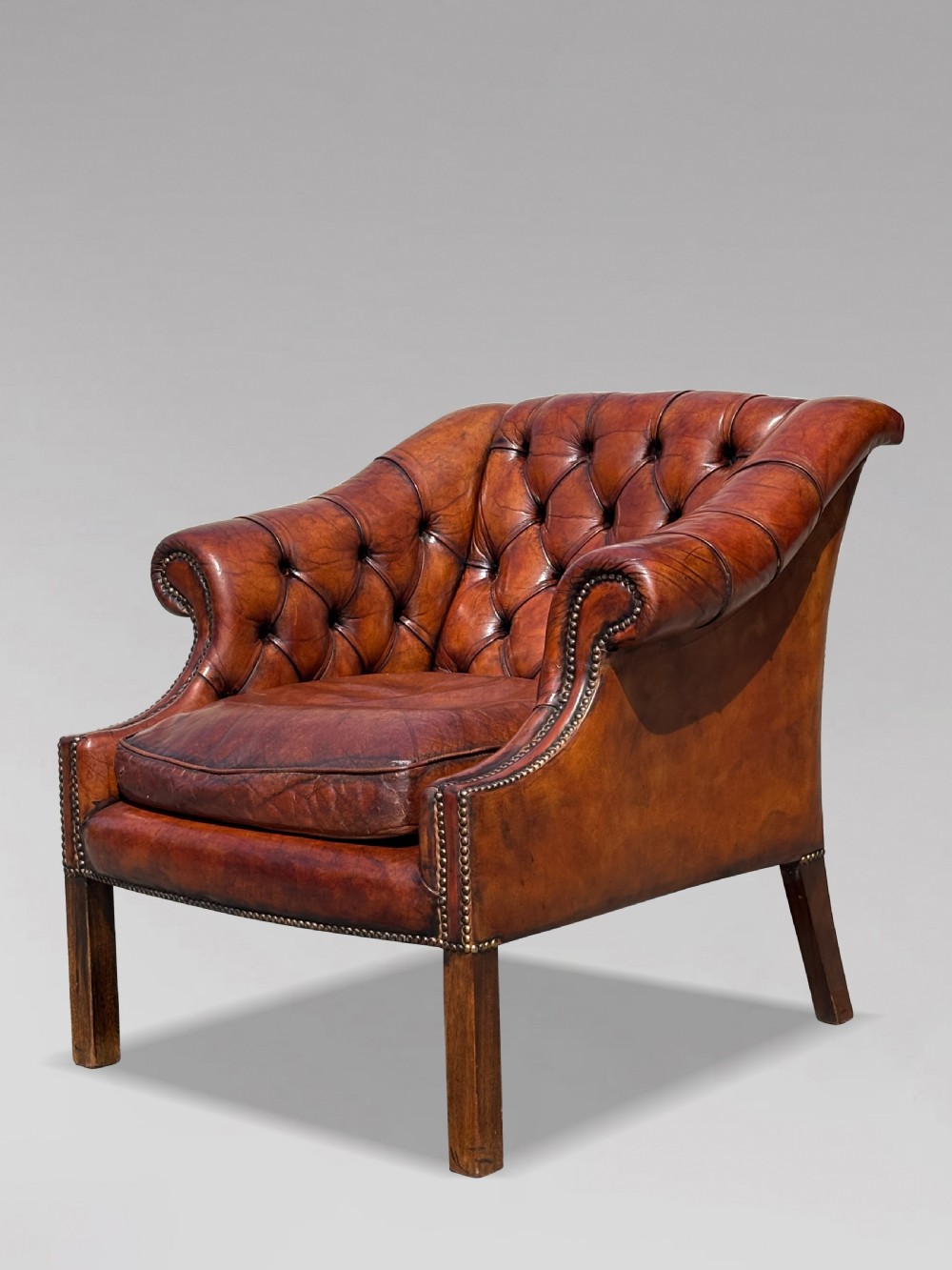 A nineteenth-century armchair upholstered in deep-buttoned brown leather with brass stud trimming along the arms and front rail, set on square wooden legs. View X