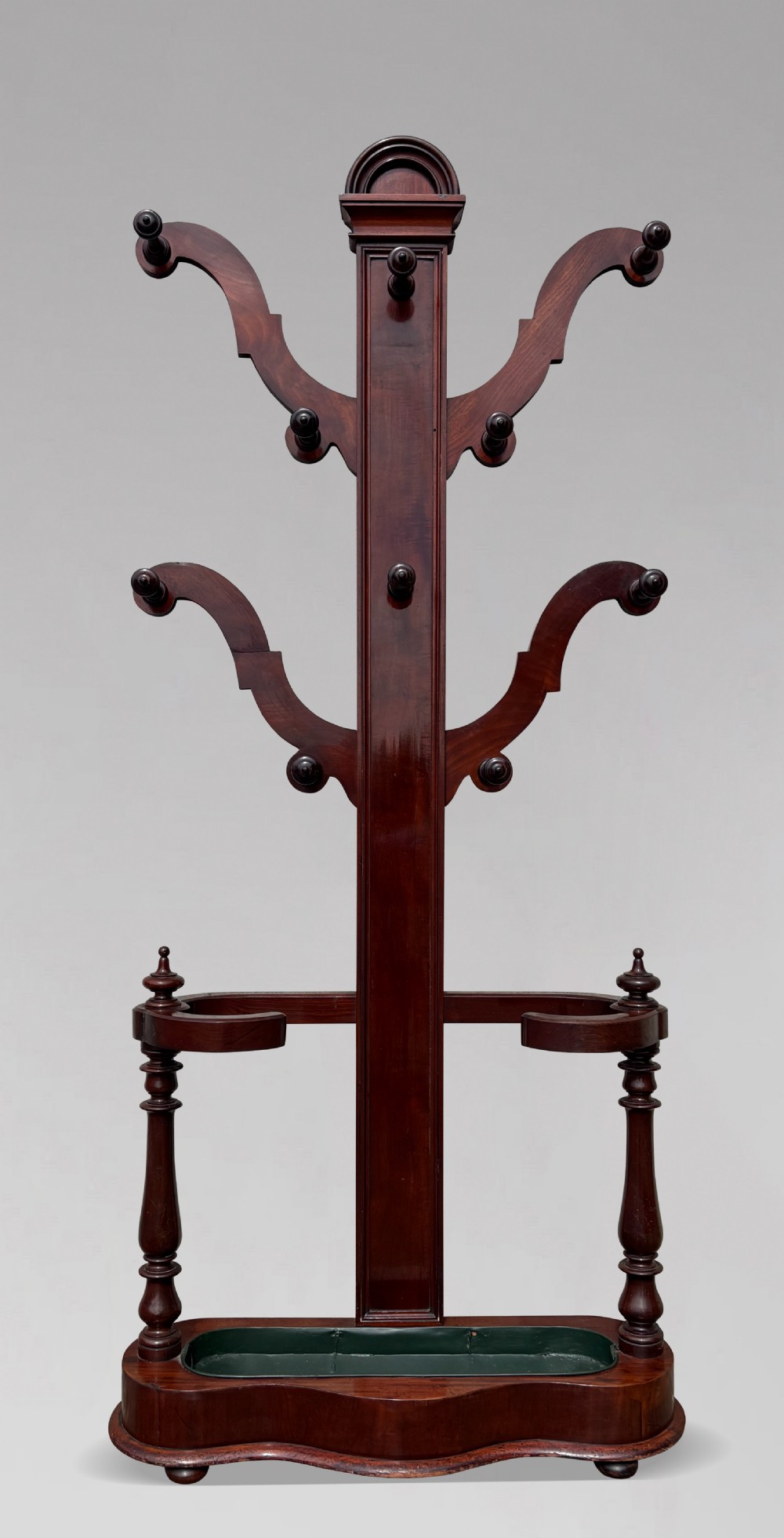 A 19th-century Victorian mahogany hall stand with carved coat pegs, turned supports, and an umbrella base featuring a green drip tray.